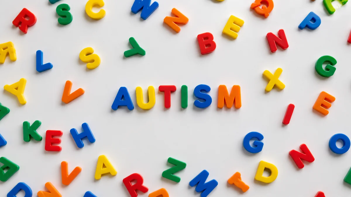 Colourful magnetic alphabet letters spelling AUTISM, surrounded by scattered letters on a white background.